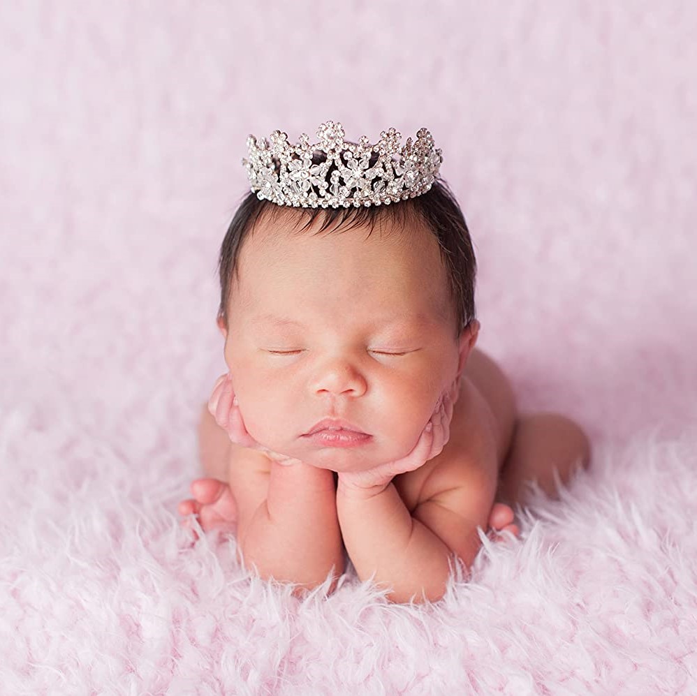 beautiful baby wearing a crown sleeping on a pink background